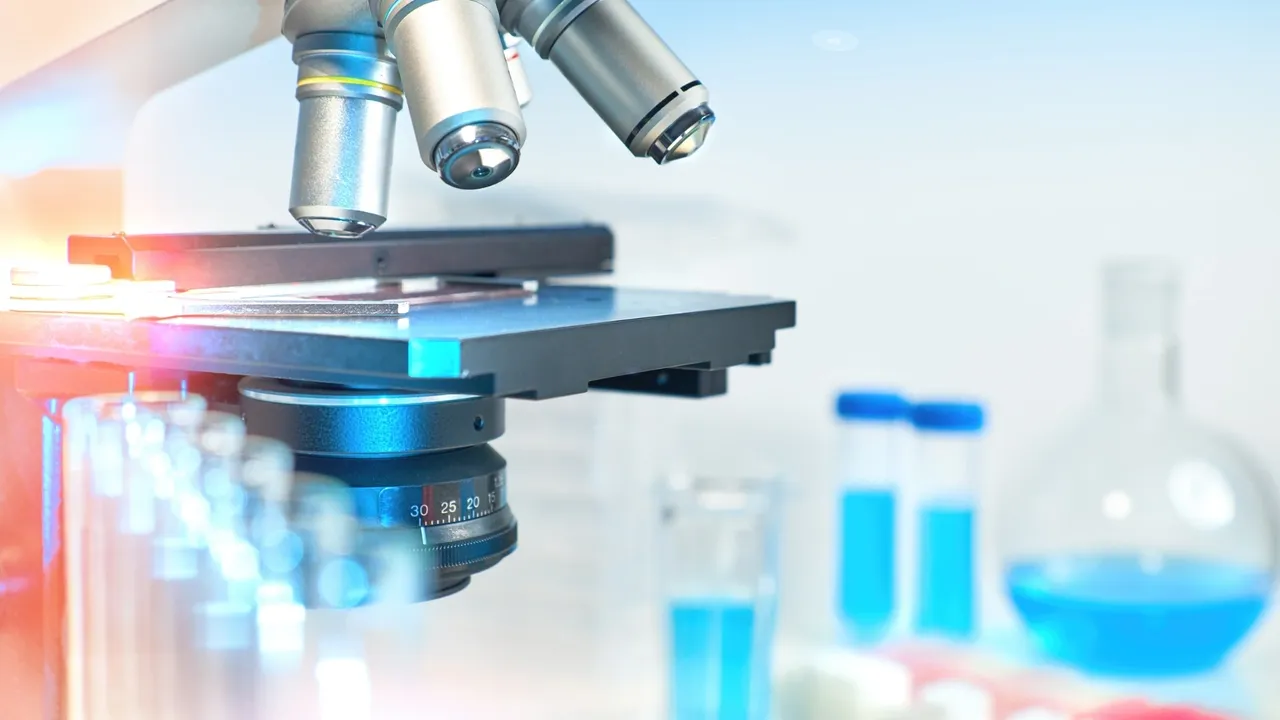 Laboratory microscope with blue-tinted lighting and blurred scientific glassware in the background