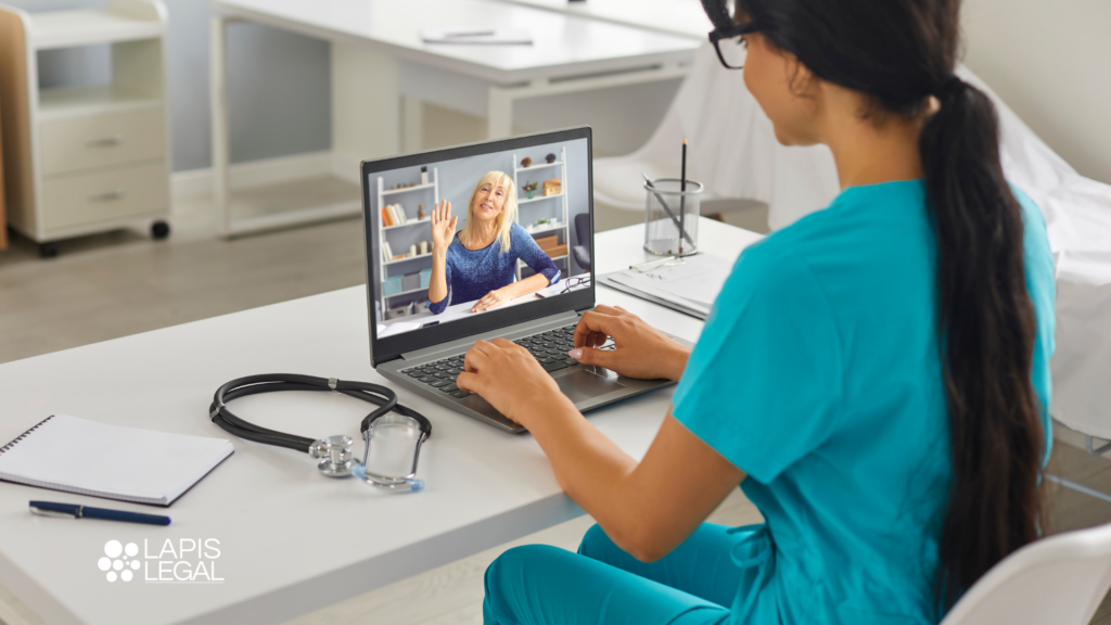 Healthcare professional in blue scrubs on a video call with a patient on a laptop, with a stethoscope on the desk nearby, lapis legal logo